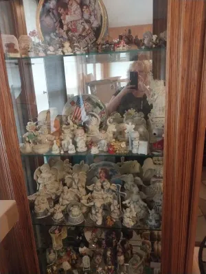 Wooden curio cabinet with glass shelves filled with a large collection of porcelain figurines, including Precious Moments and...