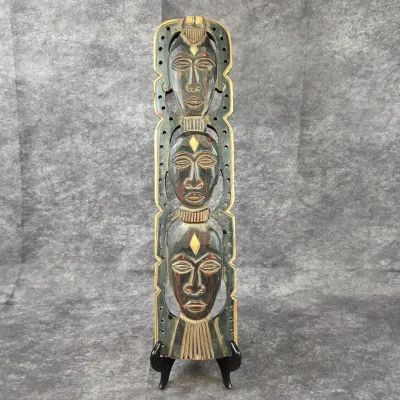 Hand-carved wooden wall plaque featuring three stacked tribal-style masks with painted accents, displayed on a black stand.