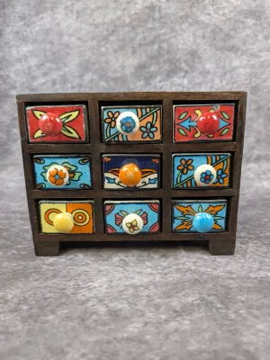 Miniature wooden chest featuring nine small drawers, each decorated with hand-painted ceramic fronts in vibrant, folk-art style floral...