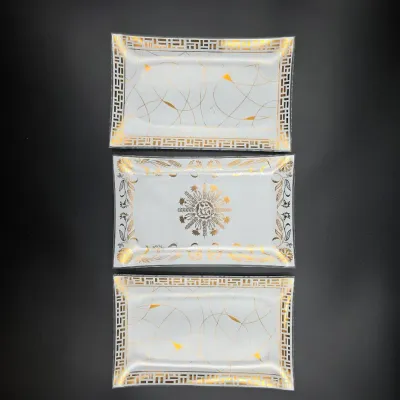 Trio of mid-century rectangular glass serving trays featuring intricate gold filigree designs and geometric borders.