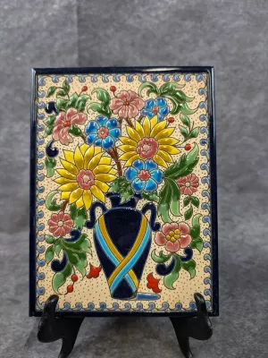Hand-painted Spanish or Mexican glazed ceramic decorative tile featuring a colorful floral arrangement in a blue vase, displayed on a...