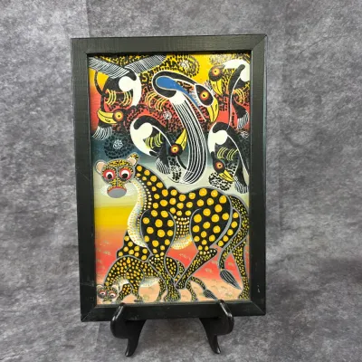Tingatinga-style painting depicting a stylized leopard and birds in vibrant colors, housed in a simple black frame.