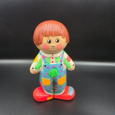 Vintage painted ceramic or plaster clown child figurine, featuring colorful overalls and reddish-orange hair.