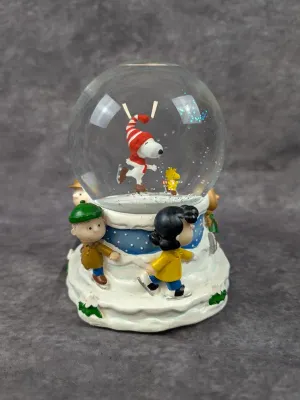 Peanuts-themed musical snow globe featuring Snoopy and Woodstock ice skating inside the globe, with Linus, Lucy, and other characters...