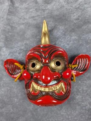 Japanese red and gold ceramic Oni mask featuring a single horn, wide ears, and golden teeth detail.