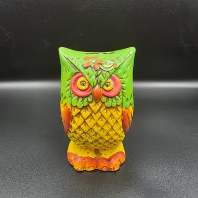 Vintage ceramic owl coin bank painted in bright green, yellow, and orange hues, featuring embossed feather textures and floral accents.