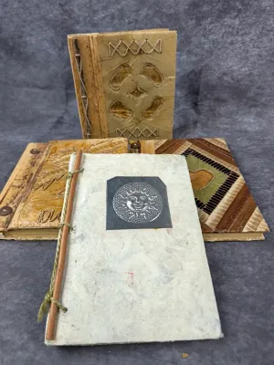 Collection of four handcrafted journals featuring natural materials, including textured handmade paper, woven leaf covers, and a...