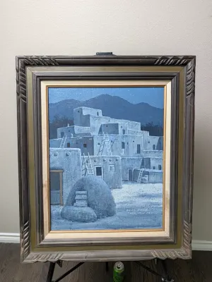 Original oil painting of Taos Pueblo at night by James Fields, housed in a heavy, carved wooden frame with a linen liner.