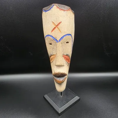 Hand-carved African tribal-style wooden mask with blue, red, and yellow painted accents, presented on a black metal display stand.