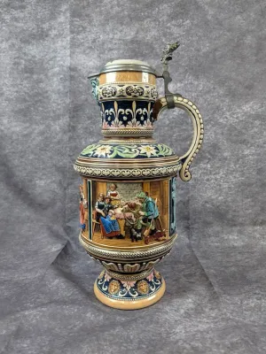 Vintage German-style ceramic beer stein pitcher featuring a detailed tavern scene, ornate floral and scrollwork bands, and a pewter lid...