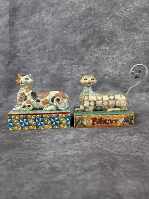 Two Jim Shore Heartwood Creek cat figurines, featuring folk-art inspired quilt patterns and colorful hand-painted details.