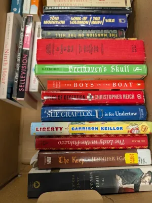 Cardboard box packed with an assortment of hardcover and paperback books, featuring titles by Sue Grafton, Toni Morrison, and Agatha...
