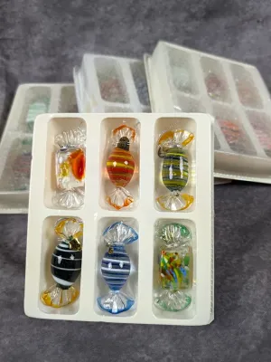 Set of colorful art glass candy-shaped Christmas ornaments in original white plastic tray packaging.