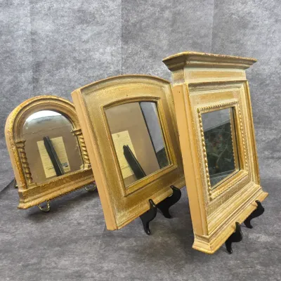 Trio of small, vintage-style tabletop mirrors with ornate gold-painted frames, displayed on individual stands.