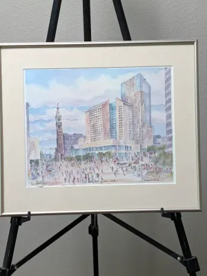 Framed and matted watercolor print depicting a bustling city plaza with modern skyscrapers and a historic clock tower, signed by the...
