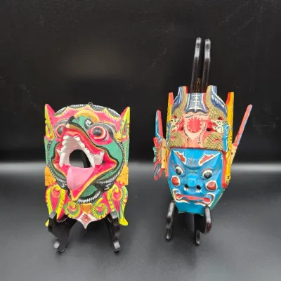 Pair of vibrant hand-carved and painted Asian decorative wooden masks mounted on black display stands.