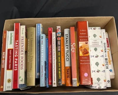 Assorted collection of cookbooks and food-related non-fiction books, including titles by Michael Pollan, Stanley Tucci, and Lidia...