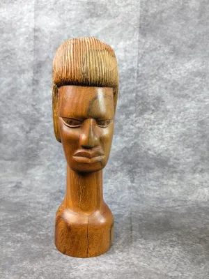 Hand-carved wooden bust sculpture featuring stylistic hair and facial details, exhibiting a visible vertical crack along the lower neck...