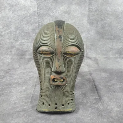 African Songye-style carved wooden mask featuring a textured, striated pattern, elongated nose, and open mouth, showing some wear and...
