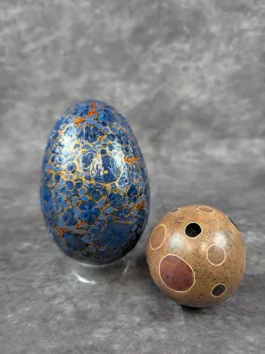 Kashmiri hand-painted papier-mâché egg with intricate blue and gold floral patterns, shown alongside a carved stone sphere with circular...