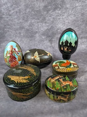 Collection of vintage Russian lacquer boxes and decorative eggs, featuring hand-painted folk art scenes, animals, and architecture.