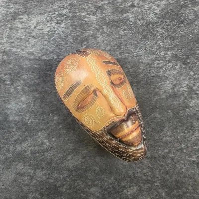Hand-carved wooden mask featuring intricate incised geometric patterns, spiral motifs, and a stylized beard.