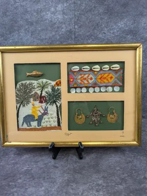 Framed Egyptian mixed-media shadowbox collage featuring embroidered fabric, cowrie shells, and traditional metal jewelry, dated 2000.