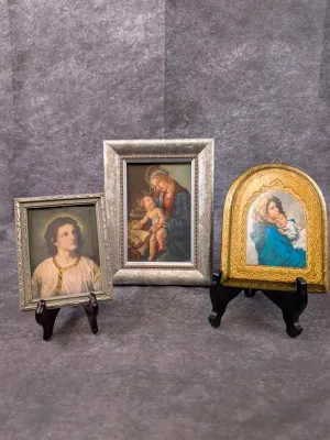 Collection of three small framed religious prints depicting various Madonna and Child and Jesus scenes, displayed on miniature stands.