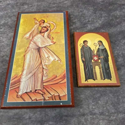 Two religious icon plaques mounted on wood, featuring St. Joseph carrying the Christ child on the left and St. Benedict with St....