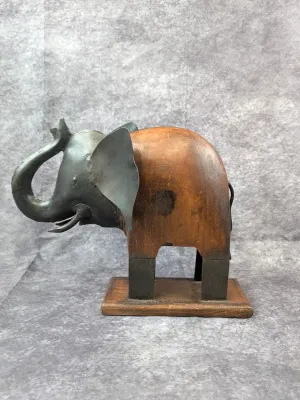 Mixed media elephant figurine featuring a carved wood body and a dark metal head and legs, mounted on a wooden base.