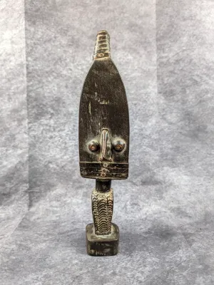Hand-carved dark wood African tribal figure, featuring stylized facial features and a textured base, showing natural surface wear.