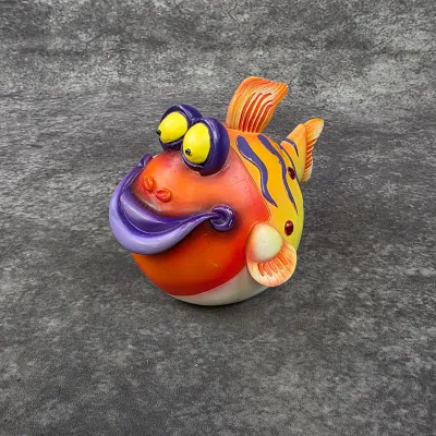 Whimsical ceramic pufferfish figurine featuring vibrant orange, yellow, and purple glaze with large cartoonish eyes and a wide smile.