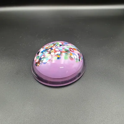 Dome-shaped art glass paperweight featuring a purple base with colorful confetti frit suspended near the top.