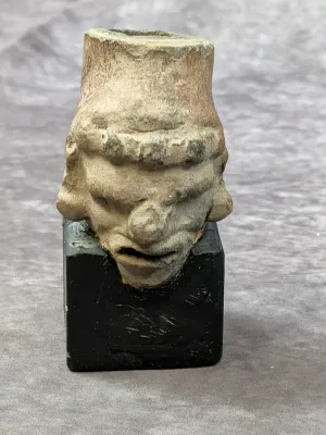 Pre-Columbian style terracotta head fragment depicting a stylized human face, mounted on a modern black display block.