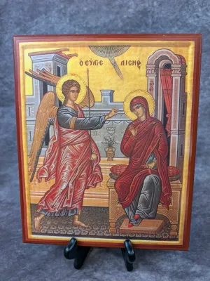 Greek Orthodox icon plaque depicting the Annunciation, mounted on a wooden block and displayed on a small black stand.