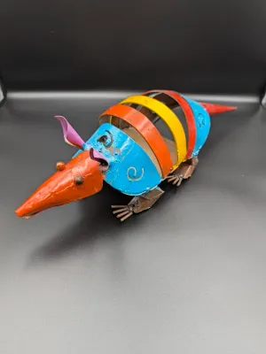 Whimsical folk art armadillo sculpture crafted from painted scrap metal bands in vibrant orange, blue, yellow, and purple.