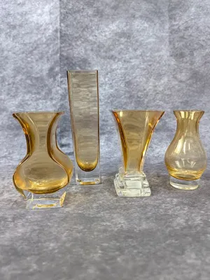 Collection of four vintage amber glass bud vases in various modern geometric and flared shapes, each featuring a clear thick glass base.