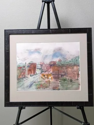Framed watercolor and ink landscape painting depicting a village scene, presented in a dark textured frame with a wide mat.