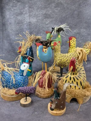 Collection of hand-painted wooden folk art chicken figurines, featuring various colors, patterns, and straw accents on wooden bases.