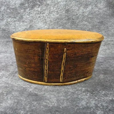 Antique oval bentwood box with a fitted lid, featuring a dark brown finish and decorative vertical lacing details.