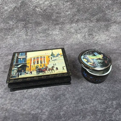 Two vintage Russian lacquer trinket boxes, including a rectangular hinged box depicting a Moscow street scene and a round box featuring a...