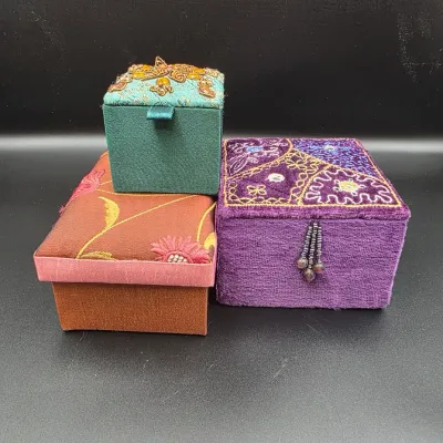 Set of three embroidered and beaded fabric keepsake boxes in various shapes and jewel tones.