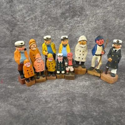 Collection of eleven vintage hand-carved and painted wooden fisherman and sailor figurines, depicting various nautical characters in rain...