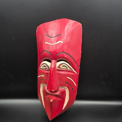 Hand-carved wooden decorative face mask painted in bright red with cream and black facial details. Features slight wear along the edges...