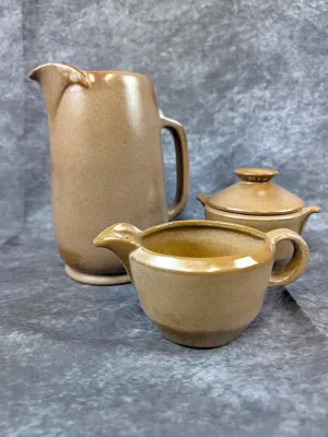 Three-piece mid-century modern ceramic set in a matte brown glaze, including a tall pitcher, a creamer, and a lidded sugar bowl.
