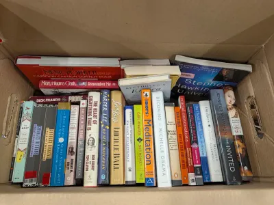 A cardboard box filled with an assortment of hardcover and paperback books, including titles by Stephen King, Michelle Obama, Harper Lee,...