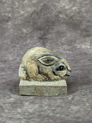 Hand-carved and painted stone rabbit figurine, depicted in a crouching position on a rectangular stone base.