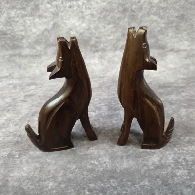 Pair of hand-carved dark wood howling wolf figurines, showing natural grain and a smooth polished finish.