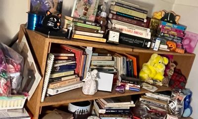 Low wooden bookshelf filled with a variety of vintage books, a yellow plush toy, a ceramic angel figurine, and other small decorative items.