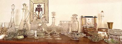 Collection of vintage glassware and barware, including crystal decanters, coupe glasses, bowls, and a small table clock, displayed on a...